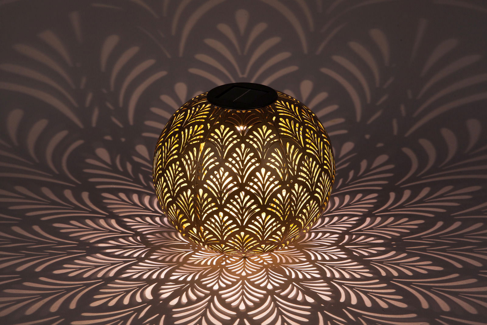 Kugelförmige Solarleuchte mit dekorativem Muster, das ein faszinierendes Licht- und Schattenspiel auf die Umgebung wirft, seitliche Perspektive.