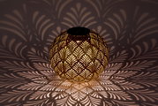 Bolvormige zonne-lamp met een decoratief patroon dat een fascinerend spel van licht en schaduw op de omgeving werpt, gezien vanaf de zijkant.