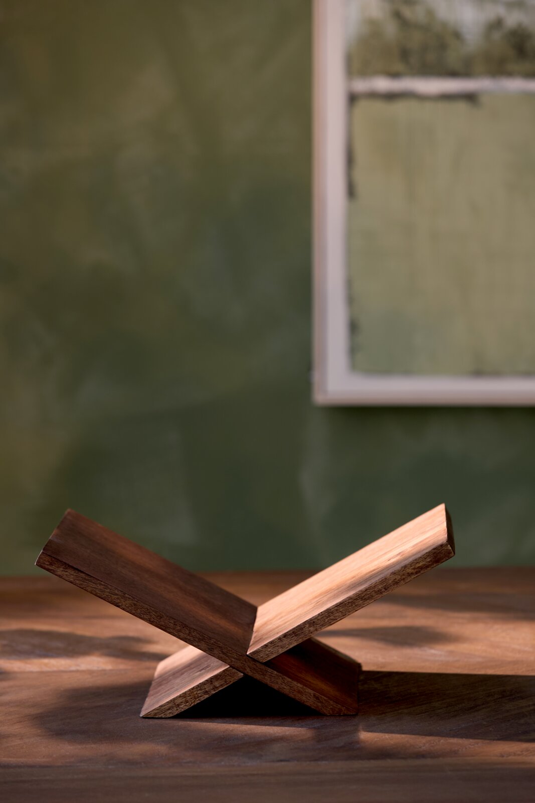 Minimalistischer klappbarer Buchständer aus dunklem Holz in seitlicher Nahansicht auf einem Holztisch