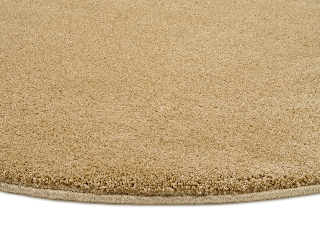 Nahaufnahme eines beigen Uni-Teppichs mit runder Form, von der Seite betrachtet.