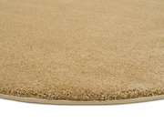 Nahaufnahme eines beigen Uni-Teppichs mit runder Form, von der Seite betrachtet.