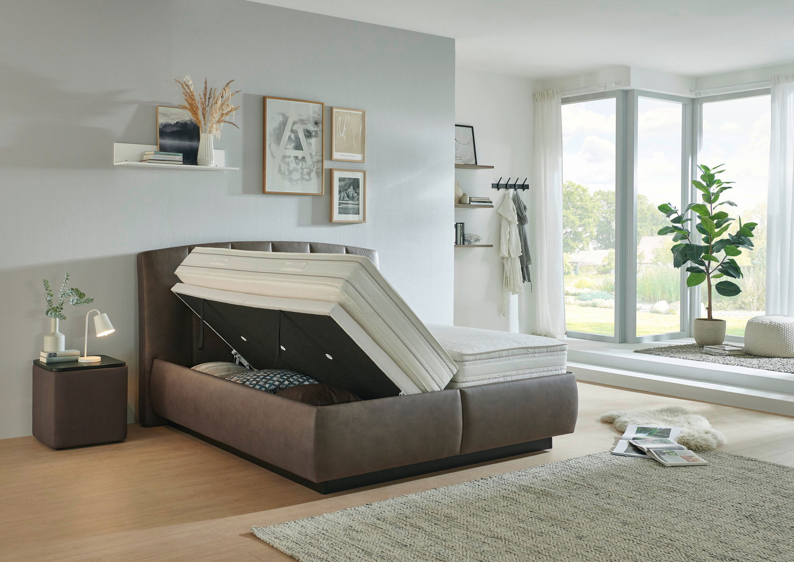 Modernes Polsterbett mit Stauraumfunktion, seitliche Perspektive, in einem hellen, stilvoll eingerichteten Schlafzimmer mit großen Fenstern.