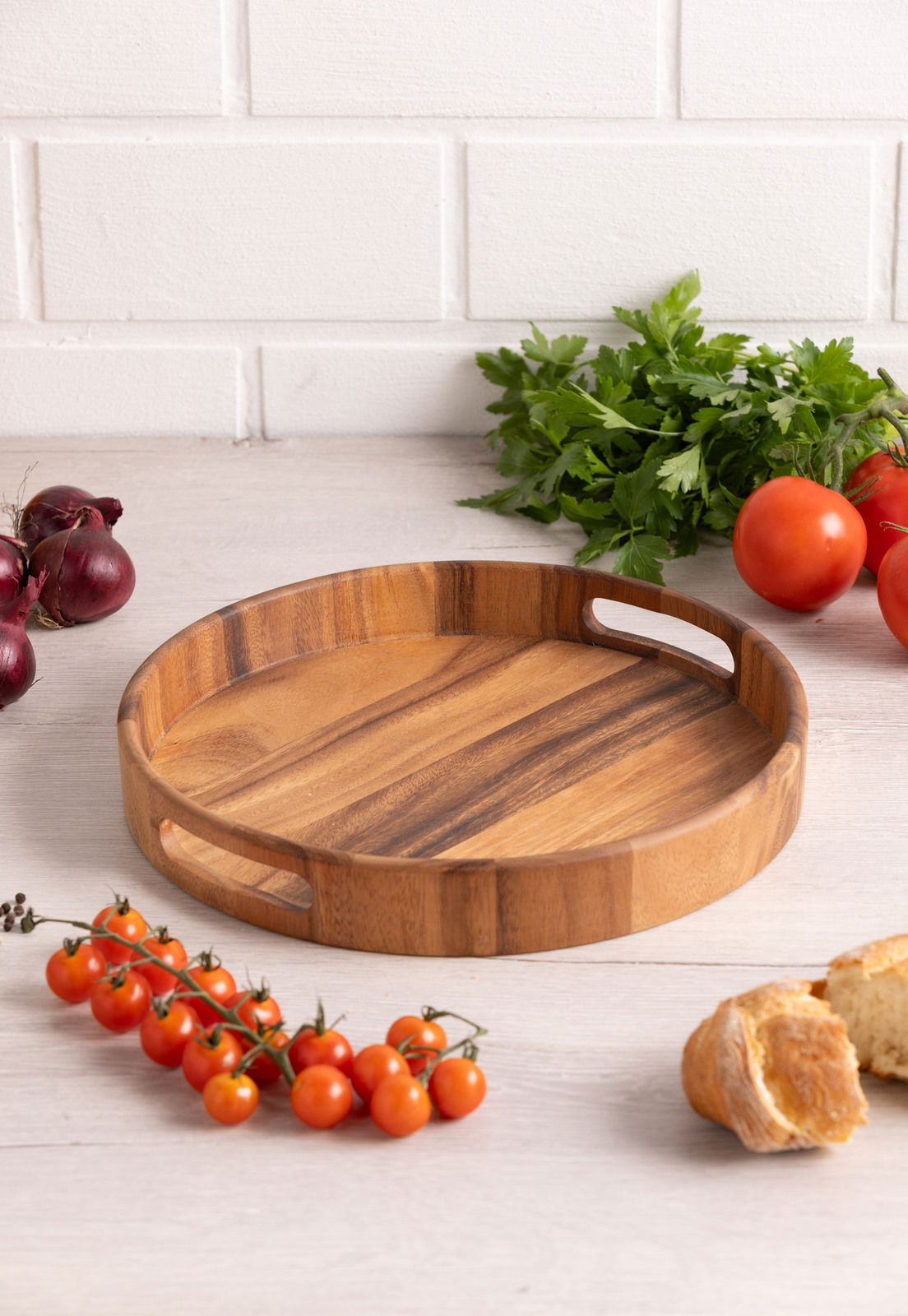 Rundes Holztablett mit Griffen, umgeben von frischen Tomaten, Zwiebeln und Petersilie, aus der Vogelperspektive fotografiert.