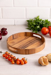 Rundes Holztablett mit Griffen, umgeben von frischen Tomaten, Zwiebeln und Petersilie, aus der Vogelperspektive fotografiert.