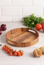 Rundes Holztablett mit Griffen, umgeben von frischen Tomaten, Zwiebeln und Petersilie, aus der Vogelperspektive fotografiert.