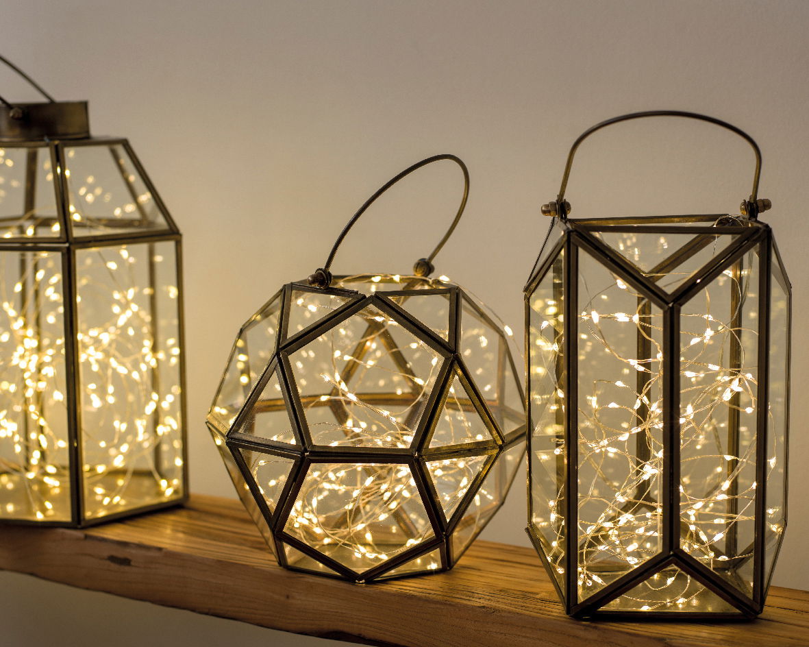 Drei geometrische Laternen mit warmweißen Micro-LED-Lichtern, auf einem Holzregal stehend, seitliche Perspektive.