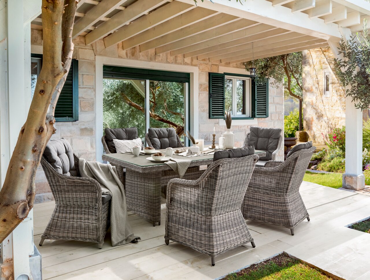 Gartensessel-Set aus grauem Rattan mit Tisch, seitliche Perspektive, dekoriert mit Geschirr und Decken.
