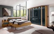 Modern houten futonbed in een stijlvolle slaapkamer met een groot raam en een kast, gezien vanaf de zijkant.