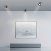 Moderne led-plafondlamp in een minimalistische ruimte, gezien van onderaf, met drie spotjes die een kunstwerk aan de muur verlichten.