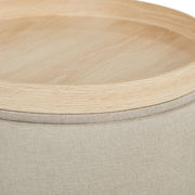 Nahaufnahme eines Hockers mit hellem Holzdeckel und beigem Stoffbezug, von oben betrachtet.