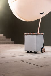 Carrycruiser Frame in seitlicher Perspektive mit Teleskopgriff und Rädern, auf einem modernen Bodenbelag vor einer Treppe.