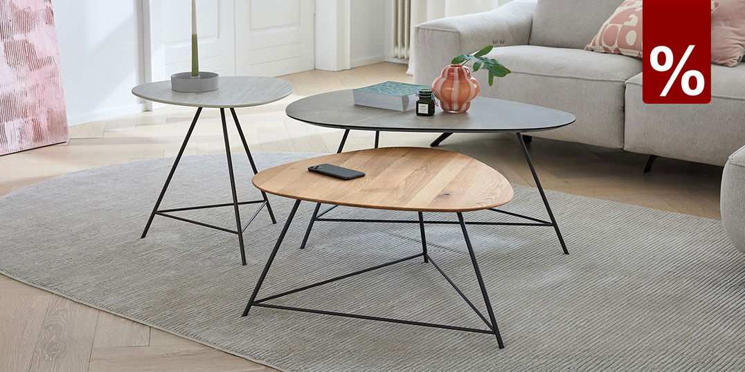Helles Wohnzimmer mit beigen Sofa, drei runden Couchtischen auf grauem Teppich und dekorativen Details