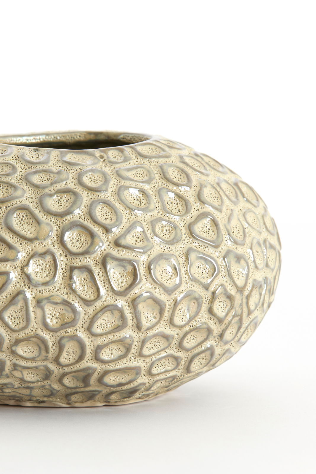 Nahaufnahme eines strukturierten, runden Teelichthalters mit organischem Muster und glänzender Oberfläche, seitliche Perspektive.