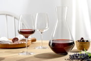 Weinset bestehend aus einer Karaffe und zwei Weingläsern, gefüllt mit Rotwein, auf einem Tisch mit einer Holzplatte und einer Schale mit Oliven, seitliche Perspektive