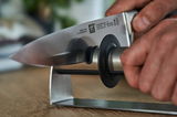 Nahaufnahme eines Messerschärfers TWINSHARP, der von einer Hand gehalten wird, während ein Messer durch den Schärfer gezogen wird.