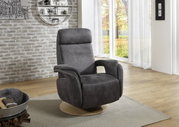 Grijze relaxfauteuil met houten onderstel, zijaanzicht, in een moderne woonkamer met grote ramen en een bakstenen muur.