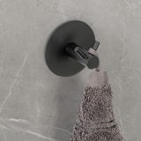 Schwarzer Wandhaken Duo Meleto an einer grauen Wand, von oben fotografiert, mit einem grauen Handtuch daran hängend.