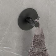 Schwarzer Wandhaken Duo Meleto an einer grauen Wand, von oben fotografiert, mit einem grauen Handtuch daran hängend.