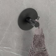 Schwarzer Wandhaken Duo Meleto an einer grauen Wand, von oben fotografiert, mit einem grauen Handtuch daran hängend.