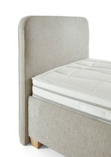 Seitliche Ansicht eines Polsterbetts mit beigem Stoffbezug und sichtbarem Kopfteil.
