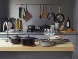 Schwarzer runder Bräter von Le Creuset, 26 cm, auf einer modernen Küchenarbeitsplatte, umgeben von Küchenutensilien und Geschirr, aus der Perspektive von vorne.