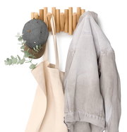 Wandgarderobe aus Holz mit Haken, an denen eine graue Mütze, eine beige Tasche und eine graue Jacke hängen. Frontalansicht.