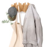 Wandgarderobe aus Holz mit Haken, an denen eine graue Mütze, eine beige Tasche und eine graue Jacke hängen. Frontalansicht.