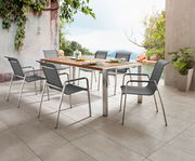 Moderner Gartentisch mit Metallrahmen und Holzplatte, umgeben von sechs stilvollen Stühlen, auf einer Terrasse mit Blick auf einen Pool und üppige Vegetation, seitliche Perspektive.