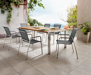 Moderner Gartentisch mit Metallrahmen und Holzplatte, umgeben von sechs stilvollen Stühlen, auf einer Terrasse mit Blick auf einen Pool und üppige Vegetation, seitliche Perspektive.