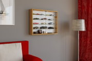 Wandvitrine mit Holzrahmen und Glasfront zur Präsentation von Modellautos, frontal aus leicht seitlicher Perspektive an einer grauen Wand