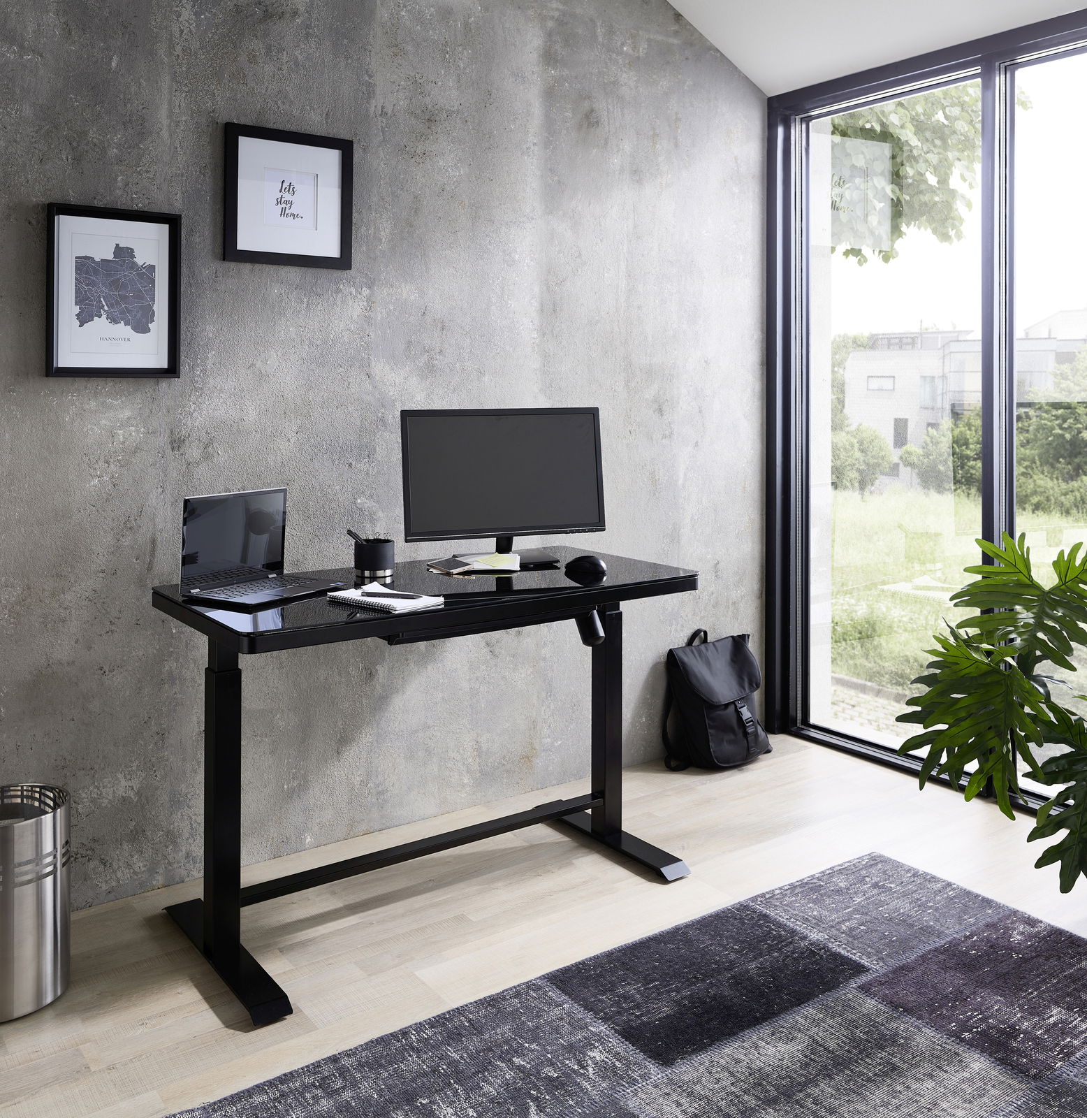 Moderner E-Schreibtisch in einem hellen Raum mit Blick auf den Garten, ausgestattet mit Monitor, Laptop und Schreibtischzubehör.