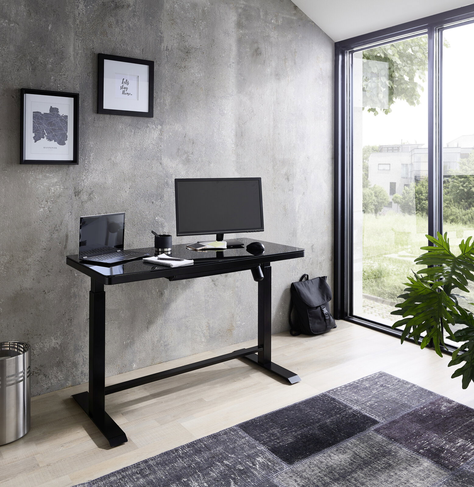 Moderner E-Schreibtisch in einem hellen Raum mit Blick auf den Garten, ausgestattet mit Monitor, Laptop und Schreibtischzubehör.