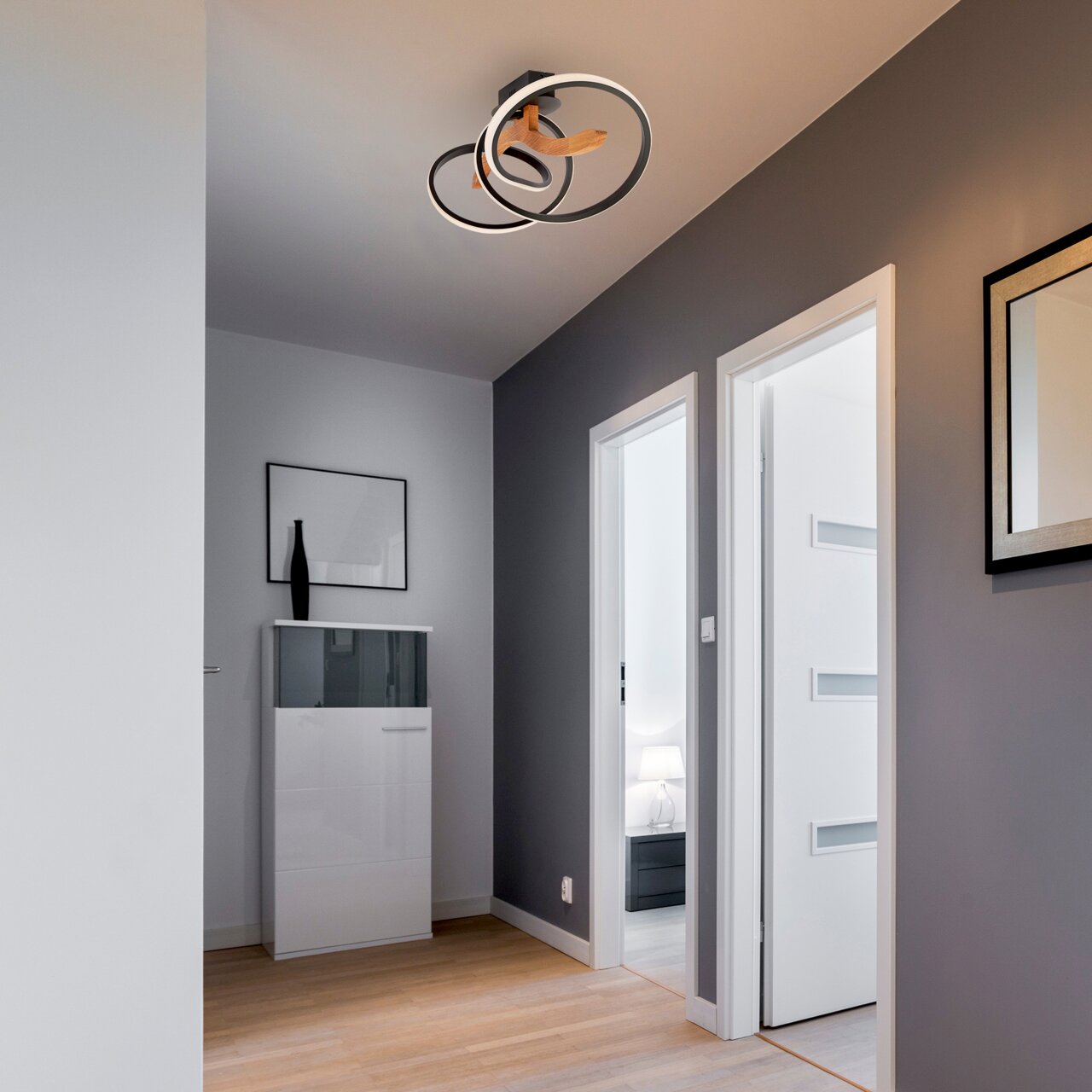 Zurbrüggen LED-Deckenleuchte ARGENTINA SWIRL Moderne LED-Deckenleuchte mit zwei ineinander verschlungenen Ringen, von unten betrachtet in einem stilvollen Flur mit grauen Wänden und Holzboden.