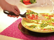 Hand hält eine Pizzaschere, die ein Stück Pizza mit Tomaten und Rucola von einem Teller schneidet. Perspektive von oben auf den Teller.