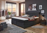 Modernes Boxspringbett in einem stilvoll eingerichteten Schlafzimmer mit Blick auf die Stadt durch große Fenster.