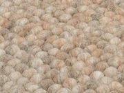 Nahaufnahme eines handgewebten Teppichs mit einer texturierten, kugelförmigen Oberfläche in natürlichen Beige- und Brauntönen.