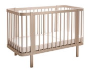 Beiges Babybett aus Holz mit Rundstäben und Matratze, freigestellt vor weißem Hintergrund, Ansicht schräg von vorne (3/4-Perspektive).