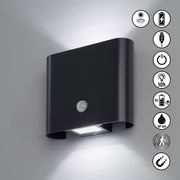 Schwarze AKKU-Wandleuchte mit Bewegungssensor, leuchtet an einer Wand. Symbole zeigen Funktionen wie USB-Aufladung, 10 Stunden Leuchtdauer und IP44 Schutz.