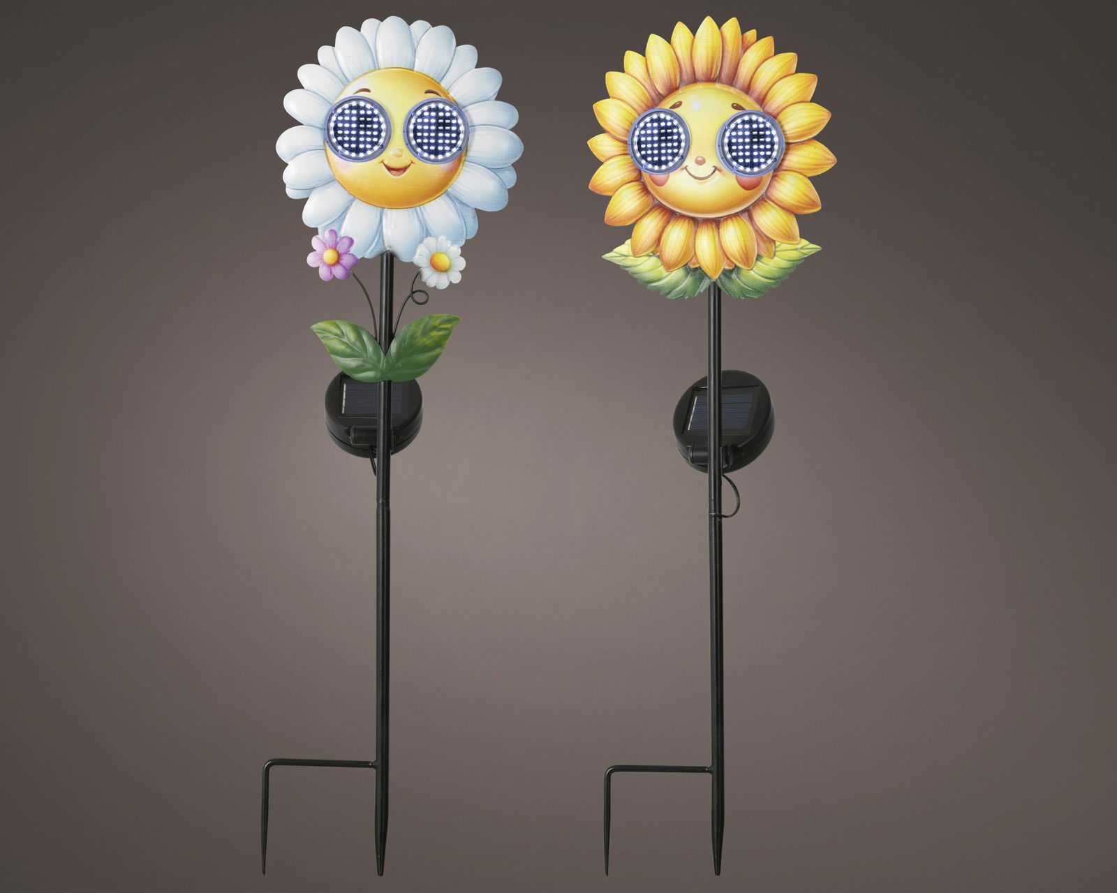 Zwei Solar Stabbeleuchten in Form von fröhlichen Blumen mit Sonnenbrillen, eine mit weißen Blütenblättern und eine mit gelben, auf einem dunklen Hintergrund. Vorderansicht.