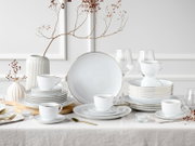 Elegantes weißes Porzellan-Tafelservice mit feiner Rillenstruktur und Goldrand, arrangiert mit Tellern, Tassen und Schalen auf gedecktem Tisch; frontale Perspektive auf das Set.