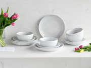 Weißes, minimalistisches Porzellan-Geschirrset mit Tellern und Schalen auf weißem Tisch, dekoriert mit pinken und gelben Tulpen; Perspektive: frontale Studioaufnahme auf Augenhöhe.