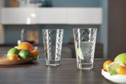 Zwei Trinkgläser Optic 300ml auf einem Tisch in einer modernen Küche, eines mit Wasser und Limettenscheibe gefüllt, im Hintergrund Obstschale mit Zitrusfrüchten, seitliche Perspektive.