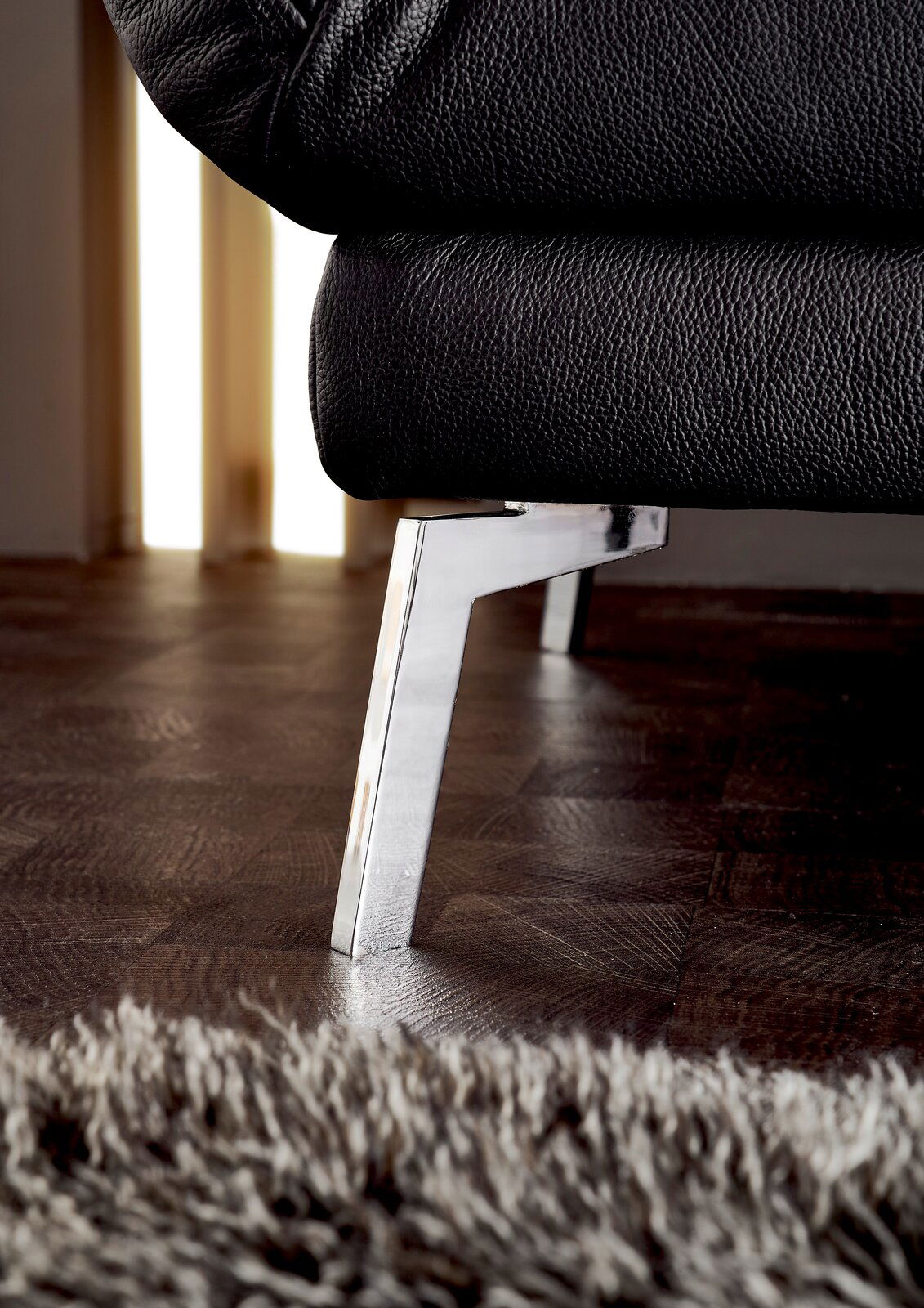 Nahaufnahme eines schwarzen Ledersofas mit verchromtem Metallfuß, seitliche Perspektive.