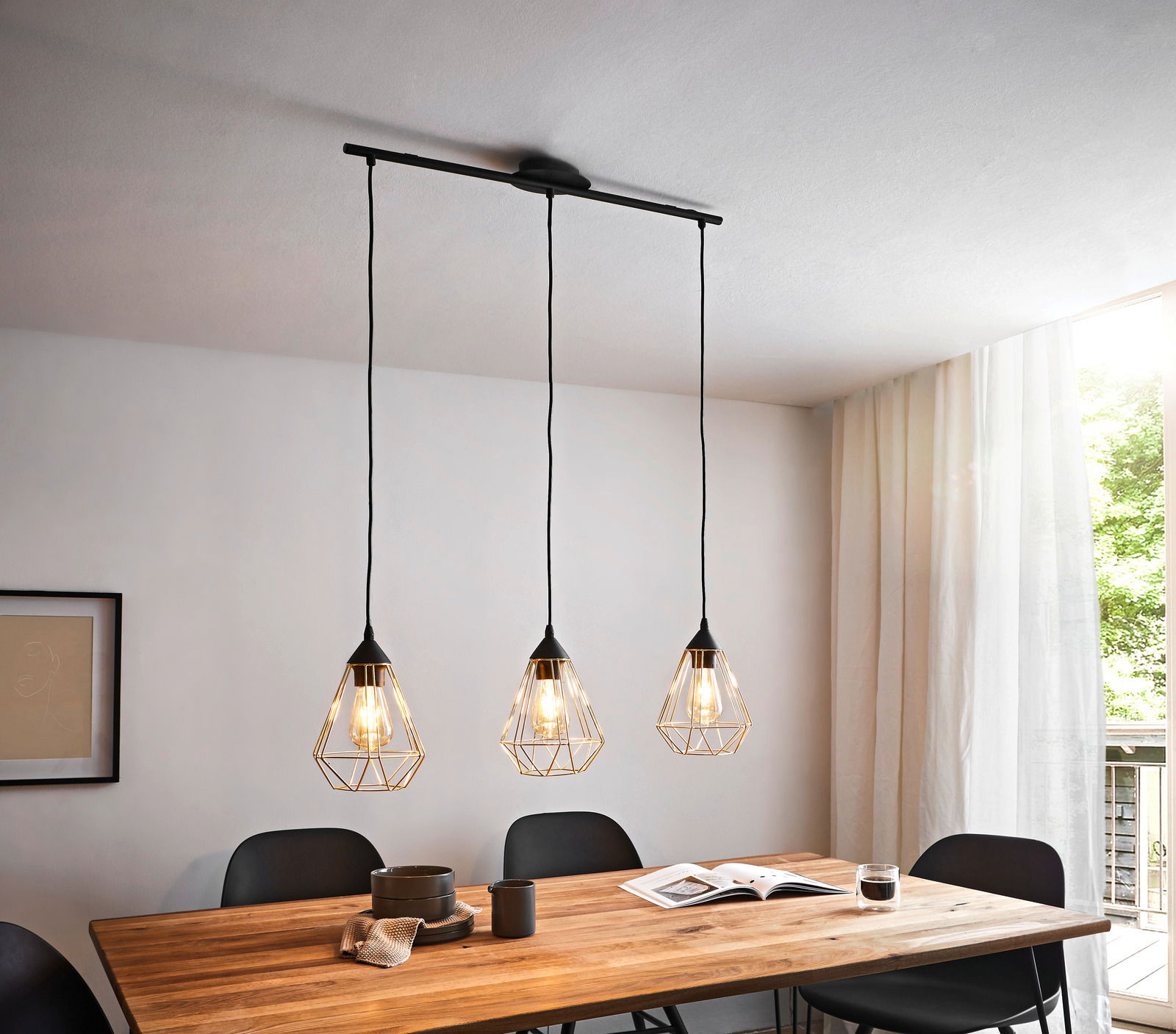 Drei Hängeleuchten mit geometrischen Drahtschirmen über einem Esstisch, seitliche Perspektive