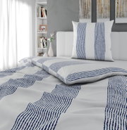 Weißes Bettwäsche-Set mit blauem Streifenmuster, Kissen und Decke auf einem Bett im modernen Schlafzimmer, Perspektive: leicht schräg von vorne in Nahaufnahme