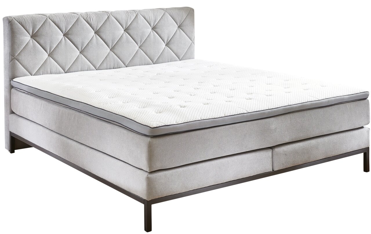 Boxspringbed in zijaanzicht met doorgestikt hoofdeinde en elegante metalen poten