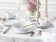 Elegant gedeckter Tisch mit weißem geripptem Porzellangeschirr (Teller, Schalen, Tassen), klaren Gläsern und goldfarbenem Besteck, dekoriert mit Kerzenständern und rosa Blumen; Perspektive: leicht erhöht aus schräger Frontansicht.