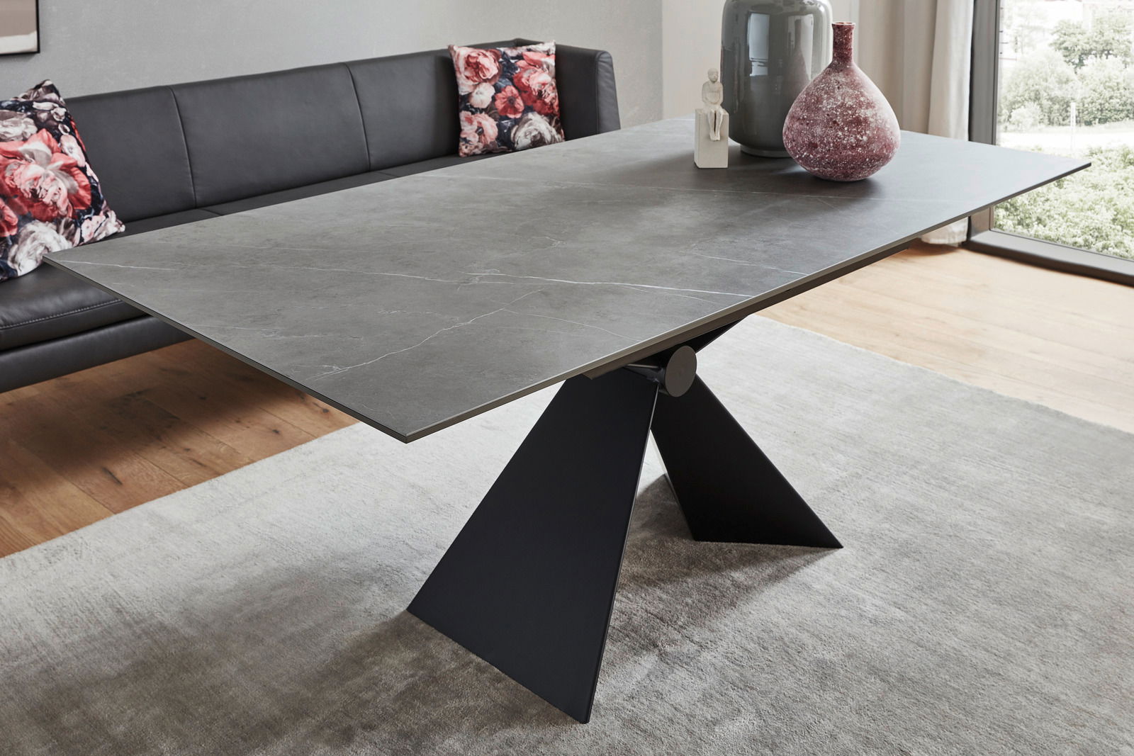 Moderner Esstisch mit grauer Steinplatte und schwarzem, skulpturalem Metallgestell, seitliche Perspektive.