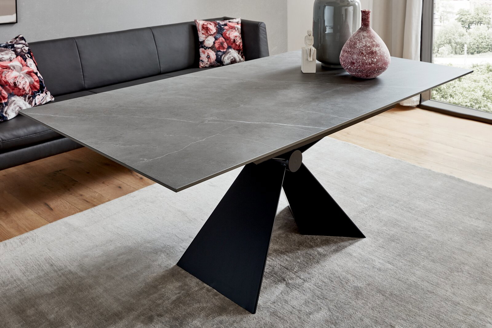 Moderner Esstisch mit grauer Steinplatte und schwarzem, skulpturalem Metallgestell, seitliche Perspektive.