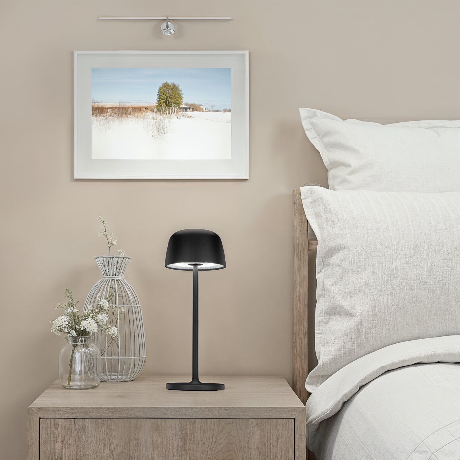 Schwarze, moderne LED-Tischleuchte mit rundem Schirm auf einem Holz-Nachttisch neben einem Bett in hellem Schlafzimmer, frontale Ansicht